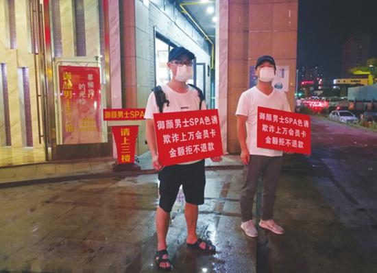 8月1日晚，“长沙御颜男仕会所”门口，两名男子戴着帽子和口罩，举牌称该会所“色 诱办卡，欺诈消费者”。潇湘晨报 图